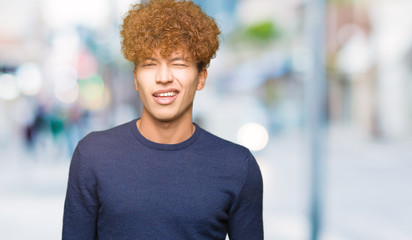 Young handsome man with afro hair winking looking at the camera with sexy expression, cheerful and...