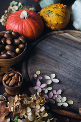 Autumn background with decorative pumpkin, acorns, nuts, greens, autumn leaves and wooden board with space for text on dark stone table