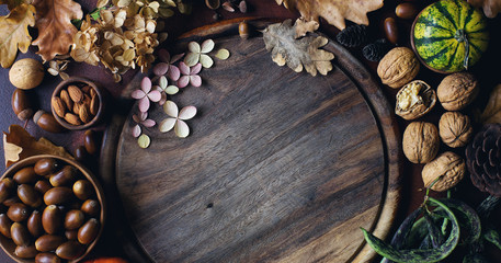 Autumn background with decorative pumpkin, acorns, nuts, greens, autumn leaves and wooden board with space for text on dark stone table