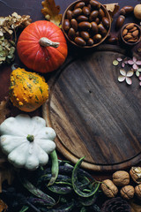 Autumn background with decorative pumpkin, acorns, nuts, greens, autumn leaves and wooden board with space for text on dark stone table