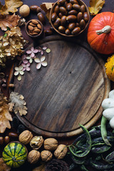 Autumn background with decorative pumpkin, acorns, nuts, greens, autumn leaves and wooden board with space for text on dark stone table