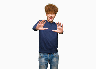 Young handsome man with afro hair afraid and terrified with fear expression stop gesture with hands, shouting in shock. Panic concept.