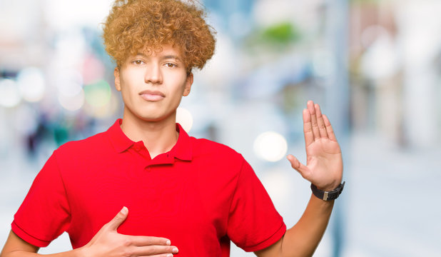 Young handsome man with afro hair wearing red t-shirt Swearing with hand on chest and open palm, making a loyalty promise oath