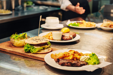 Food orders on the kitchen table in the restaurant, veggie hamburger and beef steak with fried patatoes
