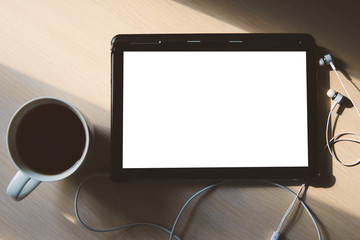 A blank tablet, earphones and a cup of tea on the wooden table. Pic in soft colors is perfect for your fall concept. Business and education background. Flat lay, copy space, view from above.