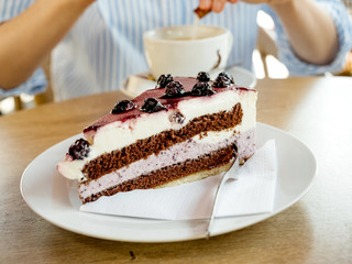 Delicious German cake Schwarzwald kirshetarten with woman pouring sugar in the coffee cappuccino