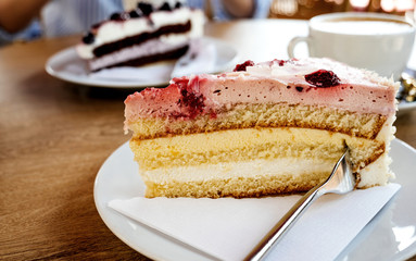 Close-up image of delicious German cake with strawberry, sour cream and mango with elegant woman eating Schwarzwald kirshetarten in the background reading a magazine