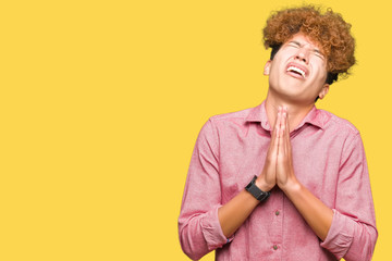 Young handsome business man with afro hair begging and praying with hands together with hope expression on face very emotional and worried. Asking for forgiveness. Religion concept.
