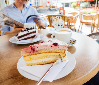 Delicious German cake with strawberry, sour cream and mango with elegant woman eating Schwarzwald kirshetarten in the background reading a magazine - square image