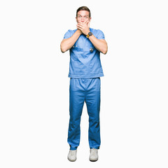 Handsome doctor man wearing medical uniform over isolated background shocked covering mouth with hands for mistake. Secret concept.