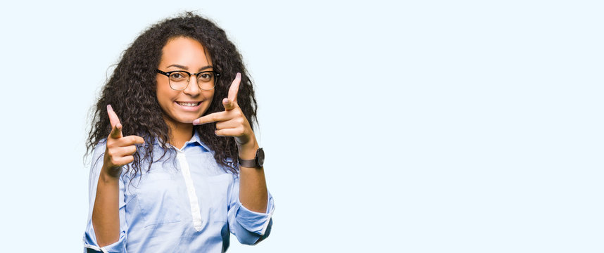 Young beautiful business girl with curly hair wearing glasses pointing fingers to camera with happy and funny face. Good energy and vibes.