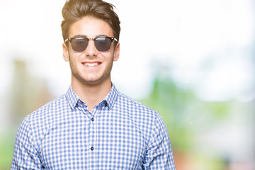 Young handsome man wearing sunglasses over isolated background with a happy and cool smile on face. Lucky person.