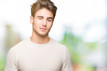 Young handsome man over isolated background winking looking at the camera with sexy expression,...