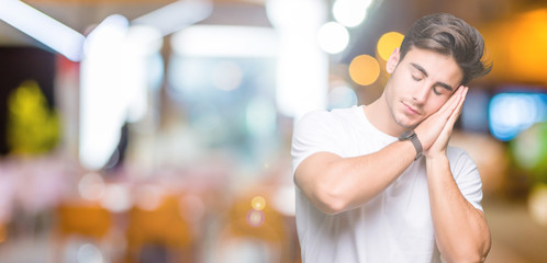 Young handsome man wearing white t-shirt over isolated background sleeping tired dreaming and posing with hands together while smiling with closed eyes.