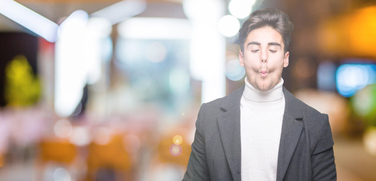 Young elegant man wearing winter coat over isolated background making fish face with lips, crazy and comical gesture. Funny expression.