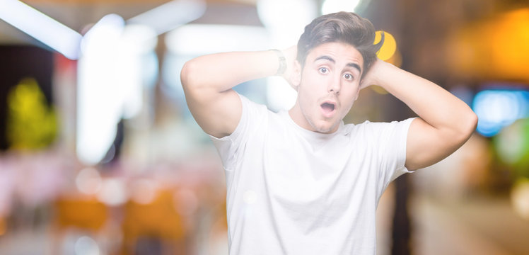 Young handsome man wearing white t-shirt over isolated background Crazy and scared with hands on head, afraid and surprised of shock with open mouth