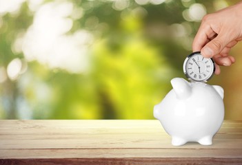 Hand depositing  clock  in piggy bank on background