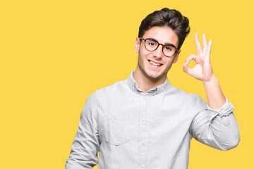 Young handsome man wearing glasses over isolated background smiling positive doing ok sign with hand and fingers. Successful expression.