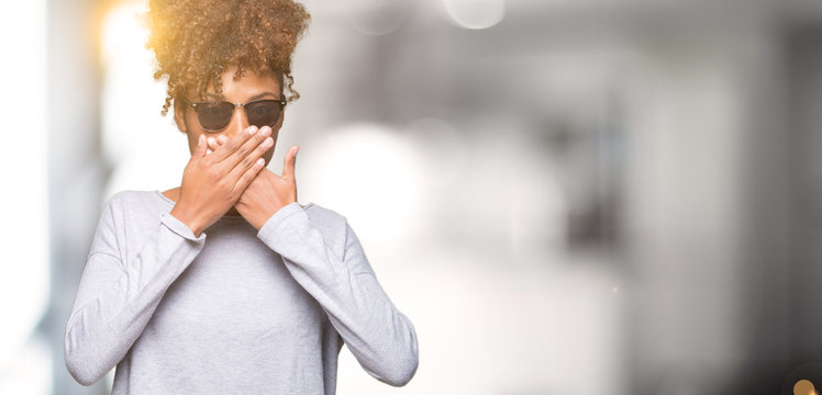 Beautiful young african american woman wearing sunglasses over isolated background shocked covering mouth with hands for mistake. Secret concept.