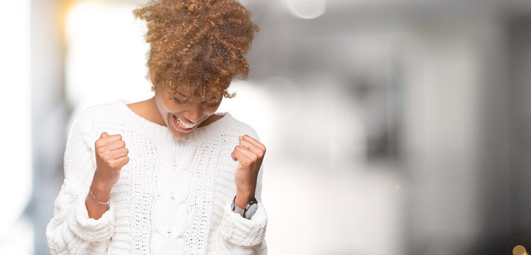 Beautiful young african american woman wearing winter sweater over isolated background very happy and excited doing winner gesture with arms raised, smiling and screaming for success. 
