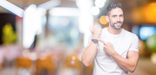 Handsome man wearing white t-shirt over night outdoors background In hurry pointing to watch time, impatience, upset and angry for deadline delay