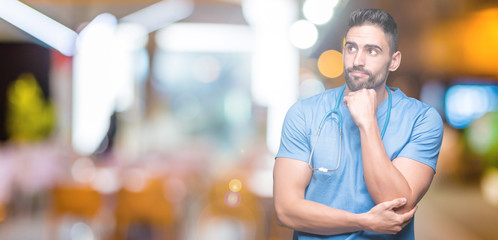 Handsome young doctor surgeon man over isolated background with hand on chin thinking about question, pensive expression. Smiling with thoughtful face. Doubt concept.