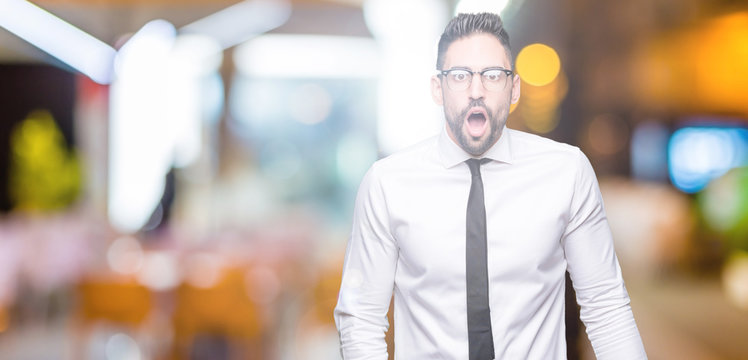 Young handsome business man wearing glasses over isolated background In shock face, looking skeptical and sarcastic, surprised with open mouth