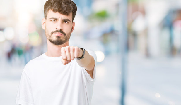 Young handsome man wearing white t-shirt over isolated background Punching fist to fight, aggressive and angry attack, threat and violence