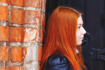 young cute girl with straight red hair near a red brick wall