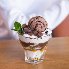 Layered dessert with banana, scoop of chocolate ice cream, whipped cream and toppings of caramel and chocolate sauce and twix pieces