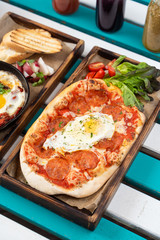 Classic rome pizza with crust, tomato sauce, spicy pepperoni and fried egg in the centre, served on summer terrace