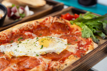 Close up of mouthwatering rome pizza with crust, tomato sauce, spicy pepperoni and fried egg in the centre