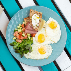 Classic hotel breakfast with sunny side up fried eggs, toasts with ham and cheese and summer salad