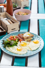Classic hotel breakfast with sunny side up fried eggs, toasts with ham and cheese and summer salad