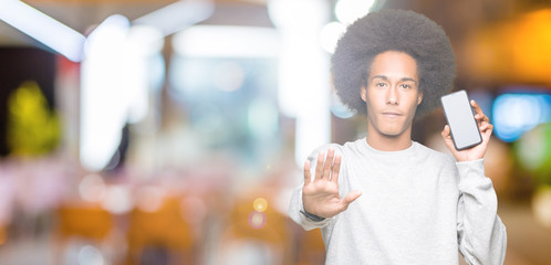 Young african american man with afro hair showing smartphone screen with open hand doing stop sign...