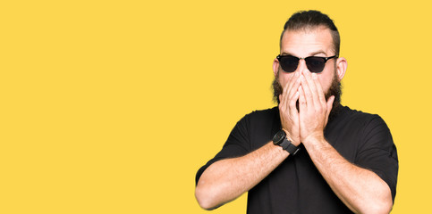 Fototapeta premium Young hipster man wearing sunglasses shocked covering mouth with hands for mistake. Secret concept.