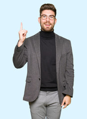 Young handsome business man wearing glasses pointing finger up with successful idea. Exited and happy. Number one.