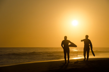 Two surfers walking on the beach at sunset