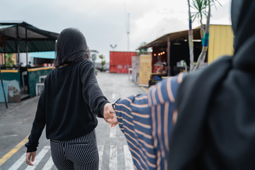back view of two friends walking together with holding hands