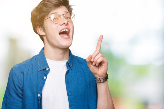 Young handsome man wearing glasses over isolated background pointing finger up with successful idea. Exited and happy. Number one.