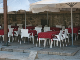 Restaurant tables and white chairs in the street outdoors in Portugal. Red tablecloth on tables.