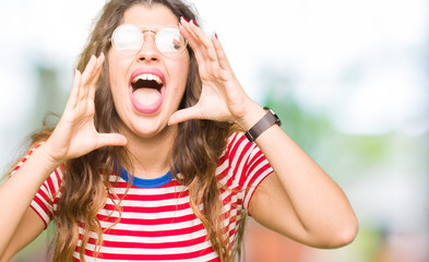 Young beautiful woman wearing glasses Shouting angry out loud with hands over mouth