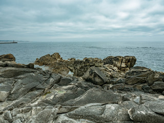 Fototapeta na wymiar Rugged, rocky shoreline. Atlantic coast of Portugal with ocean in background and cloudy sky on overcast day. Lighthouse on left in distance.