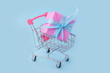 Gift pink box with blue satin ribbon in shopping cart on blue background, congratulations on Women's Day, mum's day, Valentine's day, happy birthday, Christmas