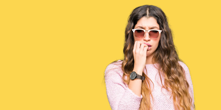 Young beautiful woman wearing sunglasses and pink sweater looking stressed and nervous with hands on mouth biting nails. Anxiety problem.