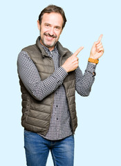 Middle age handsome man wearing winter vest smiling and looking at the camera pointing with two hands and fingers to the side.