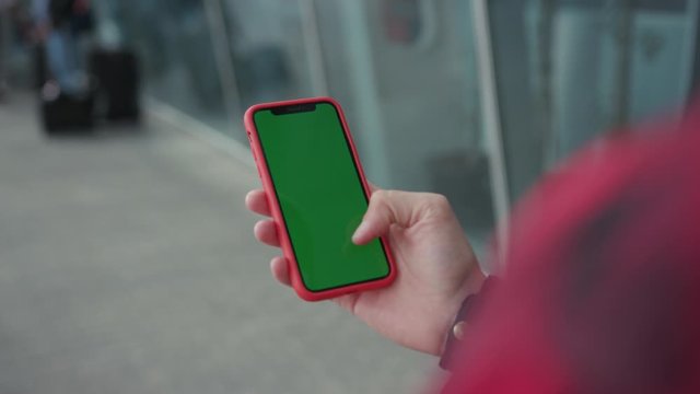 Young hands man holding a smartphone touching phone with vertical green screen red case on background walk near airport street message business male device digital equipment internet slow motion
