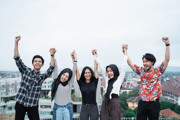 five young people hanging out and raise hand together on the building rooftop