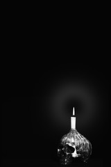 black and white of humen skull with lighting candle on dark background