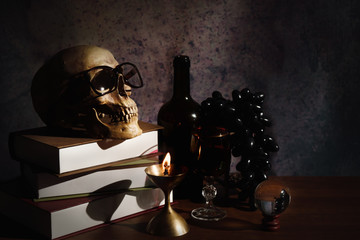 still life of humen skull on table with a glass of wine and wine bottle in a dim light room